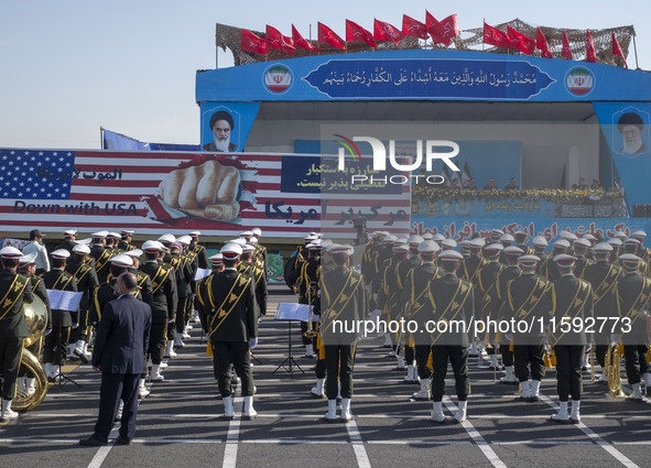 Iranian President Masoud Pezeshkian speaks with an army General while a giant anti-U.S. banner is carried by a truck during a military parad...