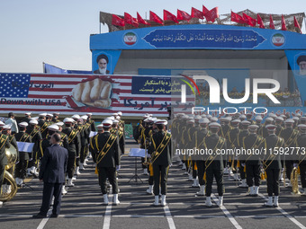 Iranian President Masoud Pezeshkian speaks with an army General while a giant anti-U.S. banner is carried by a truck during a military parad...