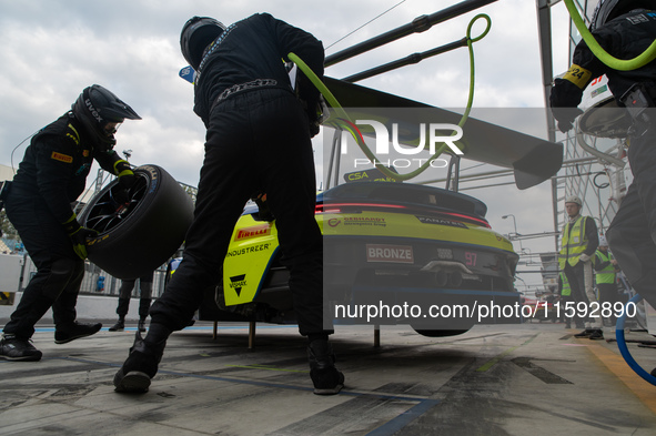 Dennis Marschall, Alexander Fach, and Dustin Blattner of the Rutronik Racing team stand next to a Porsche 911 GT3 R (992) GT car on a pit la...