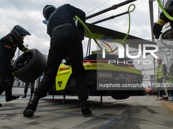 Dennis Marschall, Alexander Fach, and Dustin Blattner of the Rutronik Racing team stand next to a Porsche 911 GT3 R (992) GT car on a pit la...