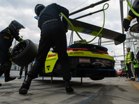 Dennis Marschall, Alexander Fach, and Dustin Blattner of the Rutronik Racing team stand next to a Porsche 911 GT3 R (992) GT car on a pit la...