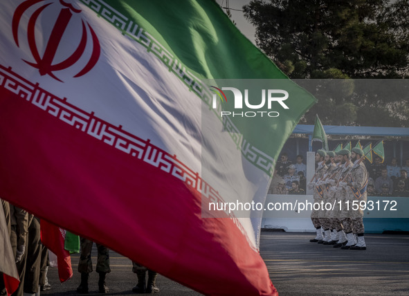 Islamic Revolutionary Guard Corps (IRGC) military personnel march next to an Iranian flag in a military parade commemorating the anniversary...