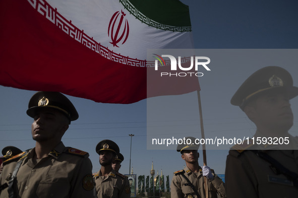 Members of the Iranian Army's land force stand at attention while one of them holds an Iranian flag during a military parade commemorating t...