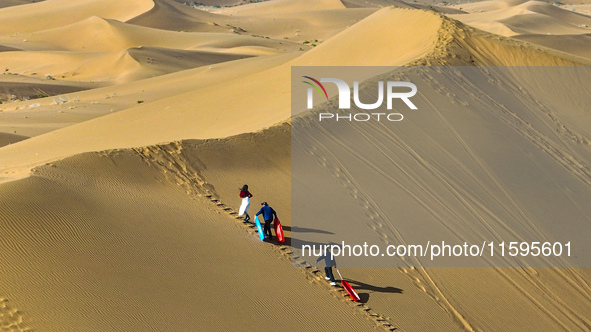 Tourists climb the sand peak to prepare for sand skating at the Jinshawan Desert tourism holiday camp in Zhangye, China, on September 21, 20...