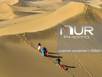 Tourists climb the sand peak to prepare for sand skating at the Jinshawan Desert tourism holiday camp in Zhangye, China, on September 21, 20...