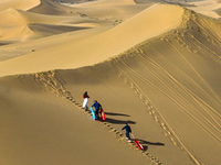 Tourists climb the sand peak to prepare for sand skating at the Jinshawan Desert tourism holiday camp in Zhangye, China, on September 21, 20...