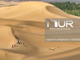 Tourists climb the sand peak to view the scenery of the desert oasis at Jinshawan Desert tourism holiday camp in Zhangye, China, on Septembe...