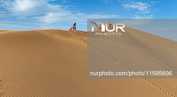 Tourists climb the sand peak to prepare for sand skating at the Jinshawan Desert tourism holiday camp in Zhangye, China, on September 21, 20...