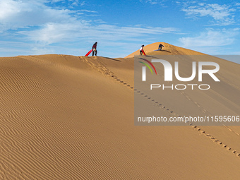 Tourists climb the sand peak to prepare for sand skating at the Jinshawan Desert tourism holiday camp in Zhangye, China, on September 21, 20...