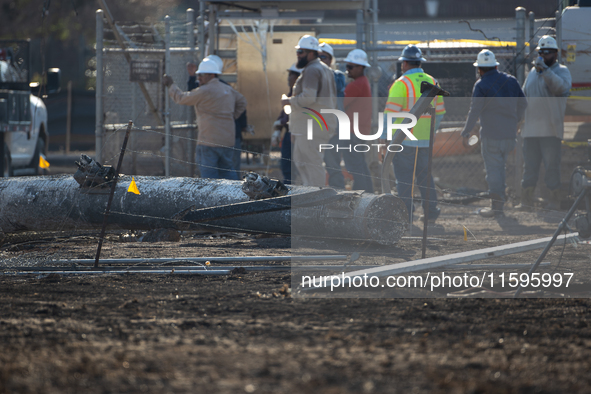 A fallen and severely burnt power line pillar is near a crew of workers following a liquefied gas pipeline explosion in a residential area o...