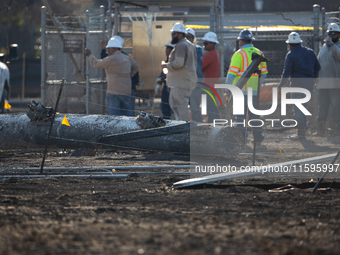 A fallen and severely burnt power line pillar is near a crew of workers following a liquefied gas pipeline explosion in a residential area o...