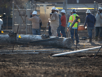 A fallen and severely burnt power line pillar is near a crew of workers following a liquefied gas pipeline explosion in a residential area o...