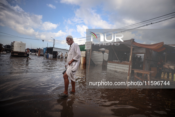 A Palestinian man walks in a puddle in rainy weather at a camp for displaced people in Khan Yunis, Gaza Strip, on September 22, 2024, amid t...