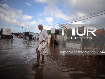 A Palestinian man walks in a puddle in rainy weather at a camp for displaced people in Khan Yunis, Gaza Strip, on September 22, 2024, amid t...