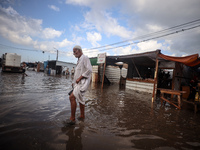 A Palestinian man walks in a puddle in rainy weather at a camp for displaced people in Khan Yunis, Gaza Strip, on September 22, 2024, amid t...