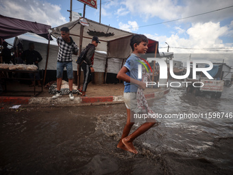 A Palestinian boy walks in a puddle in rainy weather at a camp for displaced people in Khan Yunis, Gaza Strip, on September 22, 2024, amid t...