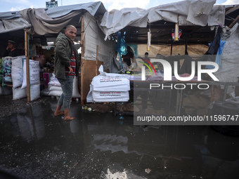 A Palestinian man walks in a puddle in rainy weather at a camp for displaced people in Khan Yunis, Gaza Strip, on September 22, 2024, amid t...