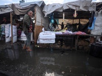 A Palestinian man walks in a puddle in rainy weather at a camp for displaced people in Khan Yunis, Gaza Strip, on September 22, 2024, amid t...