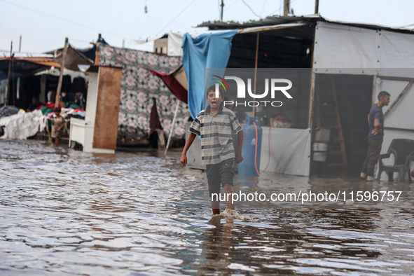 A Palestinian boy walks in a puddle in rainy weather at a camp for displaced people in Khan Yunis, Gaza Strip, on September 22, 2024, amid t...