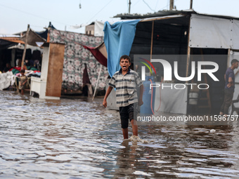 A Palestinian boy walks in a puddle in rainy weather at a camp for displaced people in Khan Yunis, Gaza Strip, on September 22, 2024, amid t...