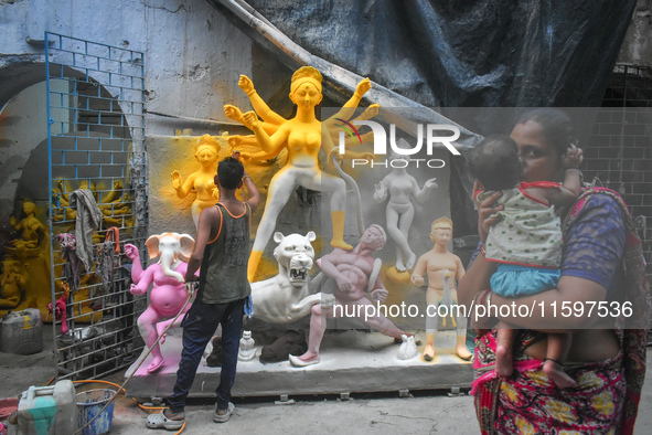 A lady kisses her child while passing next to a half-made Durga idol outside a workshop ahead of the Durga Puja festival in Kolkata, India,...