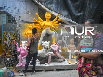 A lady kisses her child while passing next to a half-made Durga idol outside a workshop ahead of the Durga Puja festival in Kolkata, India,...