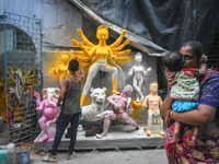 A lady kisses her child while passing next to a half-made Durga idol outside a workshop ahead of the Durga Puja festival in Kolkata, India,...