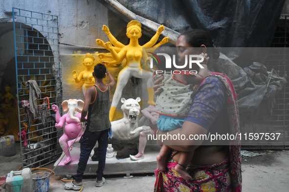 A lady carries her child and passes next to a half-made Durga idol outside a workshop ahead of the Durga Puja festival in Kolkata, India, on...