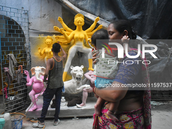 A lady carries her child and passes next to a half-made Durga idol outside a workshop ahead of the Durga Puja festival in Kolkata, India, on...