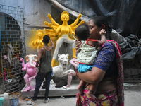 A lady carries her child and passes next to a half-made Durga idol outside a workshop ahead of the Durga Puja festival in Kolkata, India, on...