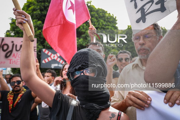 A young female demonstrator with her face covered by a bandanna raises her arm as others wave the national flag of Tunisia during a demonstr...