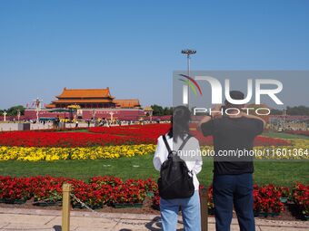 Tourists pose for a group photo in front of the flower beds at Tian 'anmen Square to celebrate the upcoming National Day in Beijing, China,...