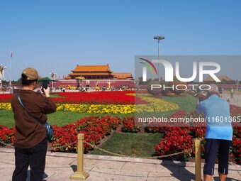 Tourists pose for a group photo in front of the flower beds at Tian 'anmen Square to celebrate the upcoming National Day in Beijing, China,...