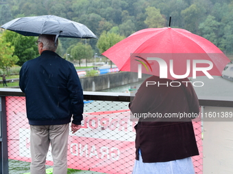 Several people with umbrellas cheer on the Lyon Kayak race on the Saone River in Lyon, France, on September 22, 2024. (