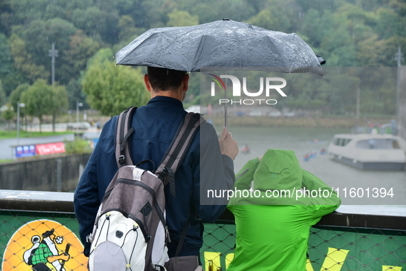 Several people with umbrellas cheer on the Lyon Kayak race on the Saone River in Lyon, France, on September 22, 2024. 