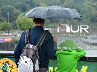 Several people with umbrellas cheer on the Lyon Kayak race on the Saone River in Lyon, France, on September 22, 2024. (