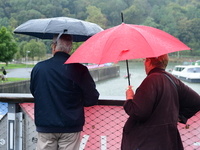 Several people with umbrellas cheer on the Lyon Kayak race on the Saone River in Lyon, France, on September 22, 2024. (