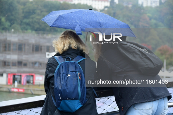 Several people with umbrellas cheer on the Lyon Kayak race on the Saone River in Lyon, France, on September 22, 2024. 