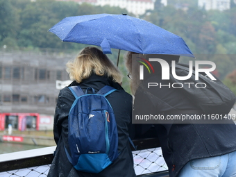 Several people with umbrellas cheer on the Lyon Kayak race on the Saone River in Lyon, France, on September 22, 2024. (