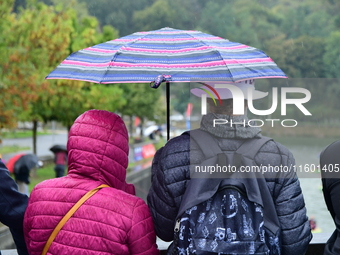 Several people with umbrellas cheer on the Lyon Kayak race on the Saone River in Lyon, France, on September 22, 2024. (