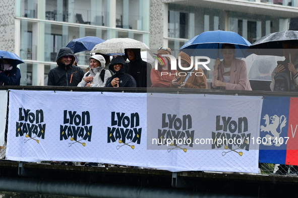 Several people with umbrellas cheer on the Lyon Kayak race on the Saone River in Lyon, France, on September 22, 2024. 