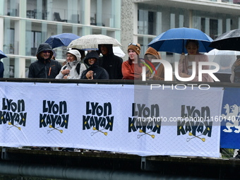 Several people with umbrellas cheer on the Lyon Kayak race on the Saone River in Lyon, France, on September 22, 2024. (