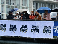 Several people with umbrellas cheer on the Lyon Kayak race on the Saone River in Lyon, France, on September 22, 2024. (