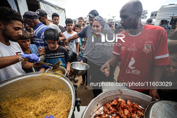 Palestinians receive cooked food rations as part of a volunteer initiative in a makeshift displacement camp in Deir Al-Balah, Gaza Strip, on...