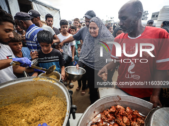 Palestinians receive cooked food rations as part of a volunteer initiative in a makeshift displacement camp in Deir Al-Balah, Gaza Strip, on...