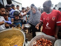 Palestinians receive cooked food rations as part of a volunteer initiative in a makeshift displacement camp in Deir Al-Balah, Gaza Strip, on...