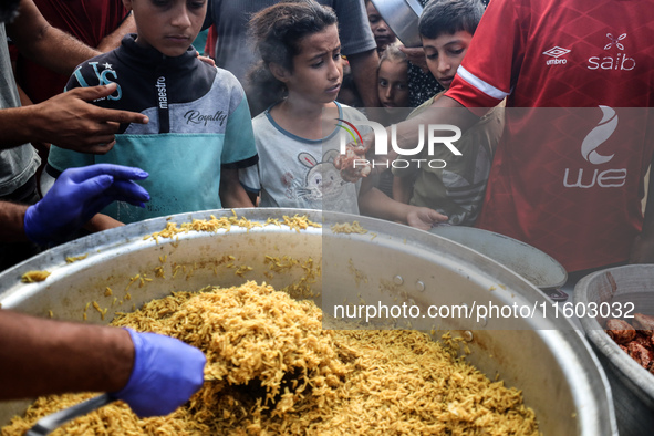 Palestinians receive cooked food rations as part of a volunteer initiative in a makeshift displacement camp in Deir Al-Balah, Gaza Strip, on...