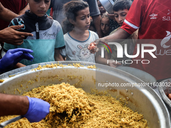 Palestinians receive cooked food rations as part of a volunteer initiative in a makeshift displacement camp in Deir Al-Balah, Gaza Strip, on...