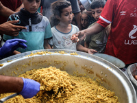 Palestinians receive cooked food rations as part of a volunteer initiative in a makeshift displacement camp in Deir Al-Balah, Gaza Strip, on...