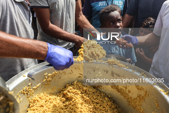 Palestinians receive cooked food rations as part of a volunteer initiative in a makeshift displacement camp in Deir Al-Balah, Gaza Strip, on...